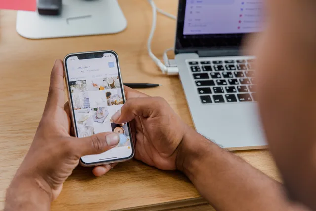 Close-up of a person working on a smartphone while using a laptop at a wooden desk. Einen Anbieterwechsel ohne Verlust wichtiger Inhalte planen