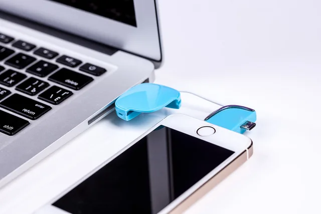 Close-up of a laptop and smartphone connected via USB cable for data transfer. Native Schnittstellen und Integrationsplattformen prüfen